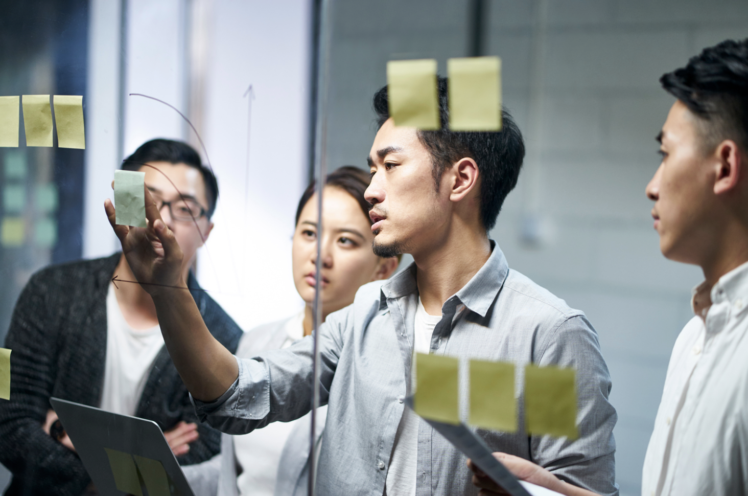 Group of people standing around a glass screen with post it notes on it.